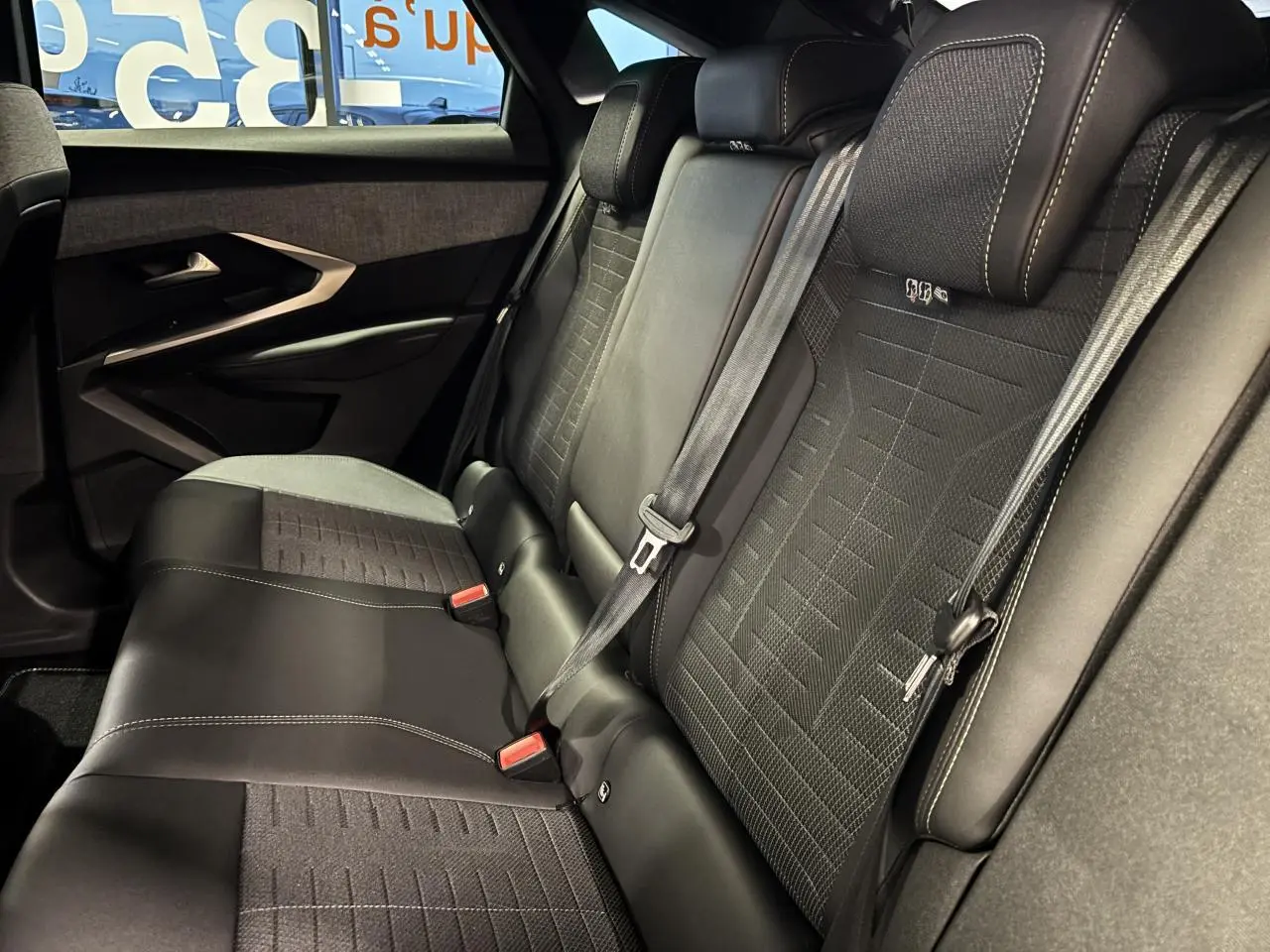 Vue intérieure des sièges arrière en tissu et cuir noir du Peugeot 3008 Hybrid 2025, avec ceinture de sécurité et porte arrière.