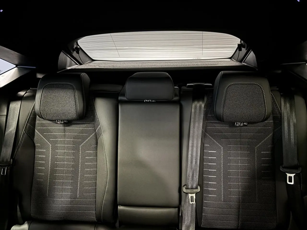 Vue arrière des sièges arrière noirs en tissu et cuir du Peugeot 3008 Hybrid 2025 avec ceinture de sécurité visible.
