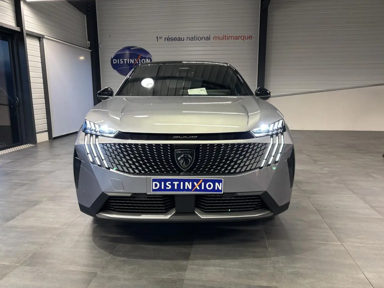 Vue de face du Peugeot 3008 gris Artense avec calandre noire laquée et feux LED à griffes allumés en intérieur showroom.