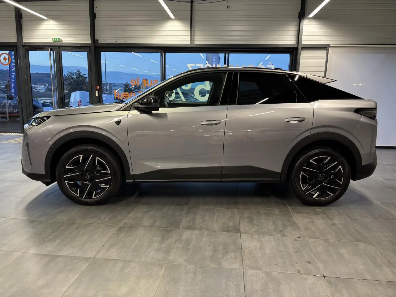 Vue de profil côté gauche d’un Peugeot 3008 gris Artense avec jantes alliage noires et toit noir dans un showroom.
