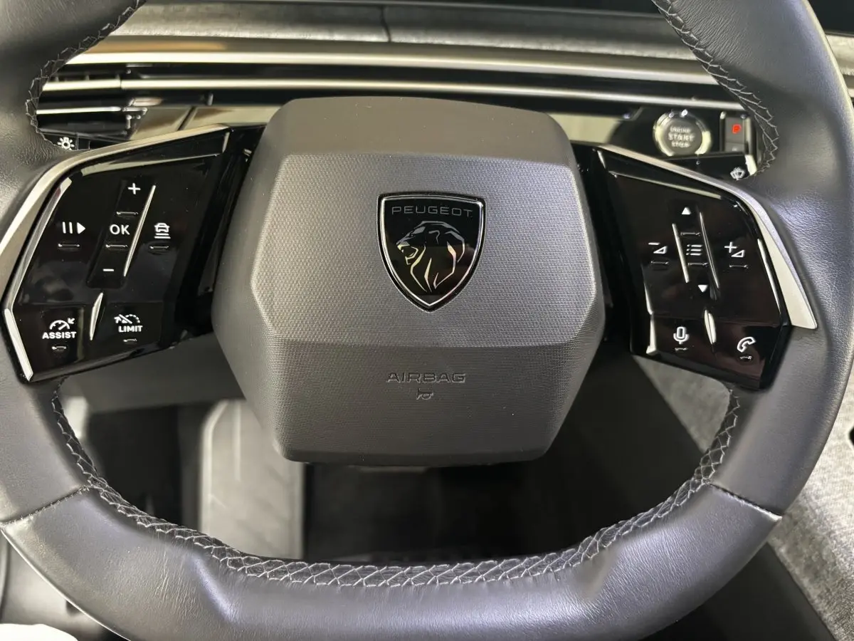 Gros plan sur le volant cuir noir du Peugeot 3008 2025 avec commandes multifonctions et bouton démarrage visible.