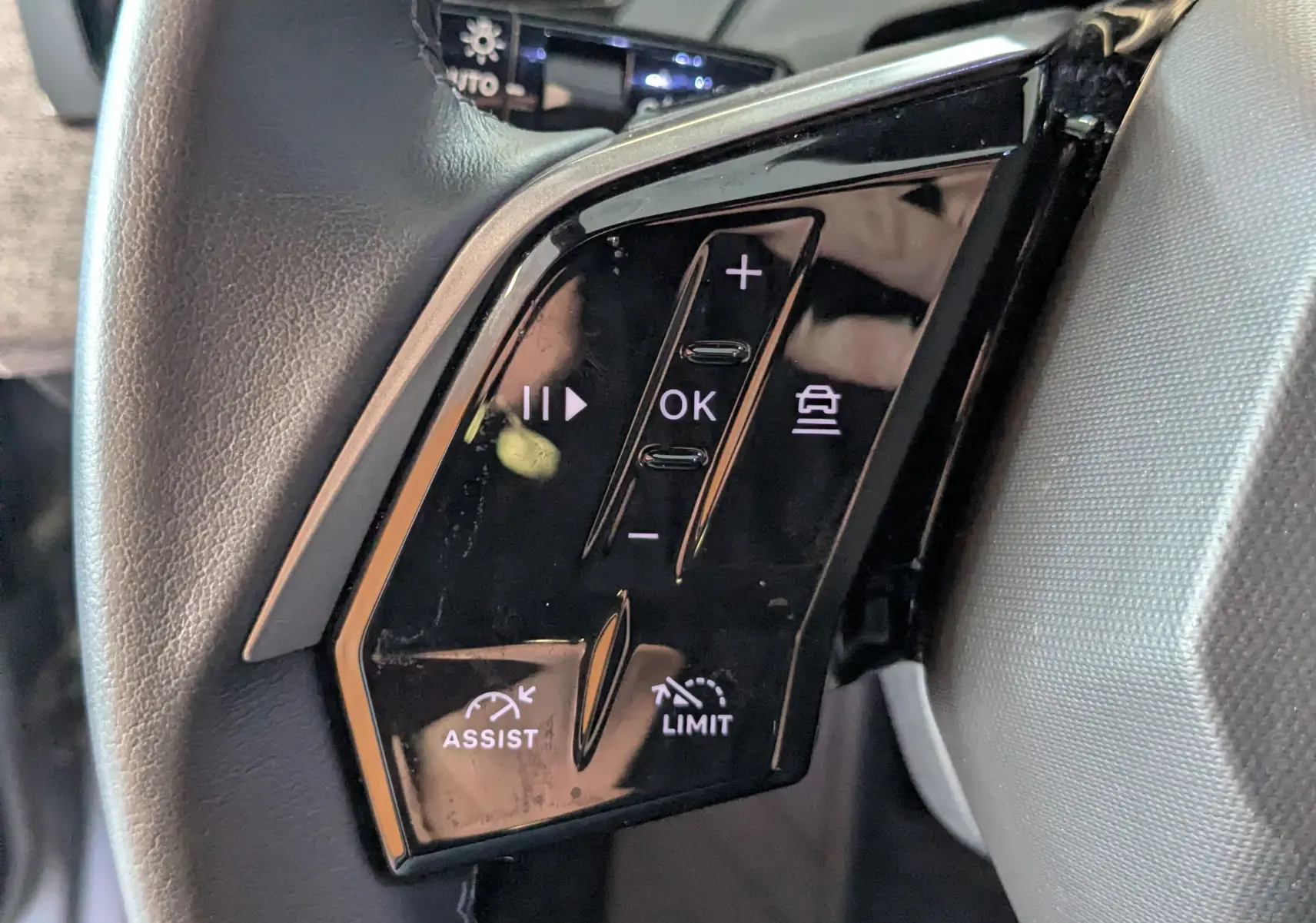 Gros plan sur les commandes noires du volant côté gauche du Peugeot 3008 gris hybride 2024, avec boutons d'assistance et limitation.