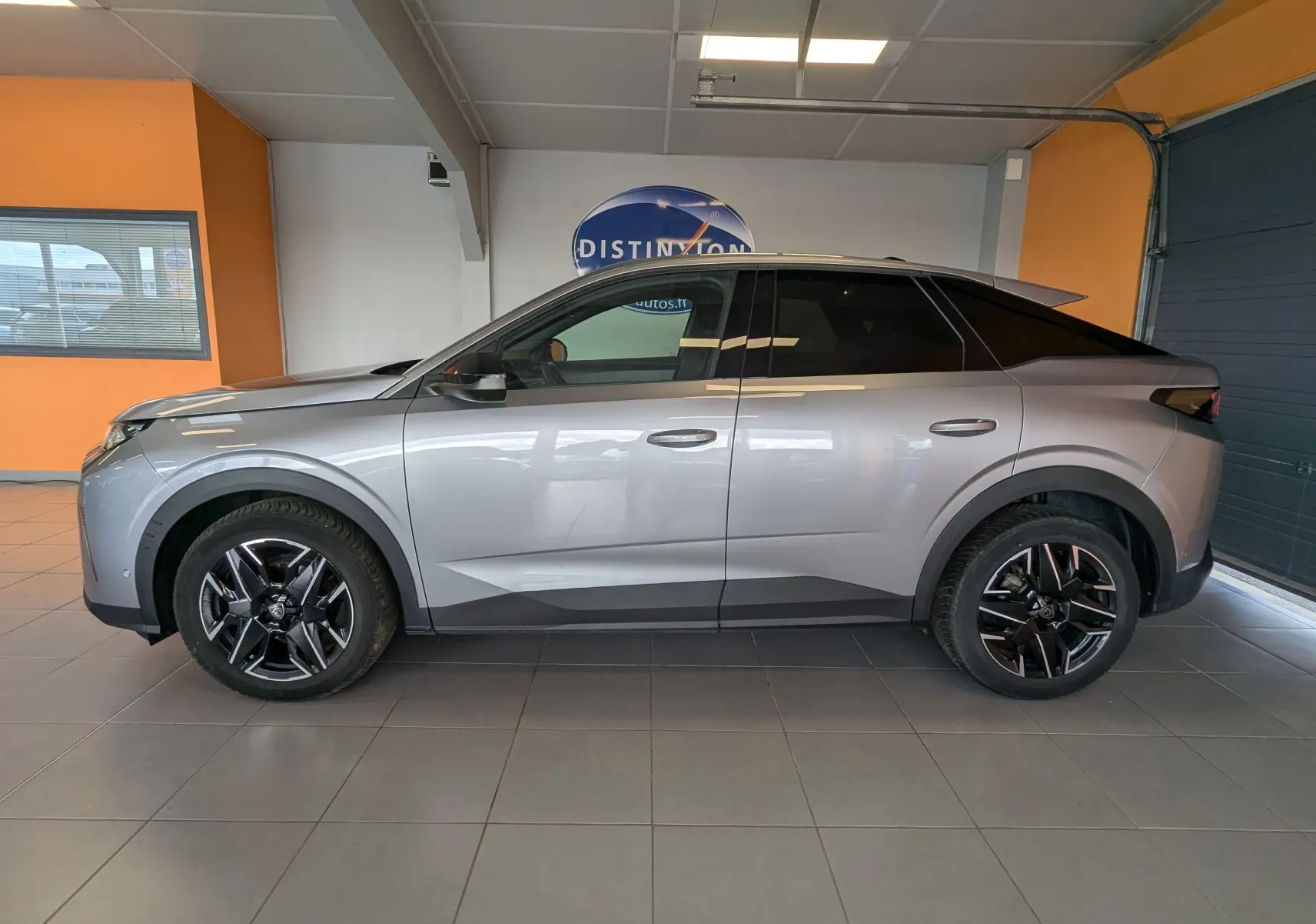 Profil côté gauche d’un Peugeot 3008 gris 2024 hybride essence, avec jantes noires et toit noir en intérieur showroom.