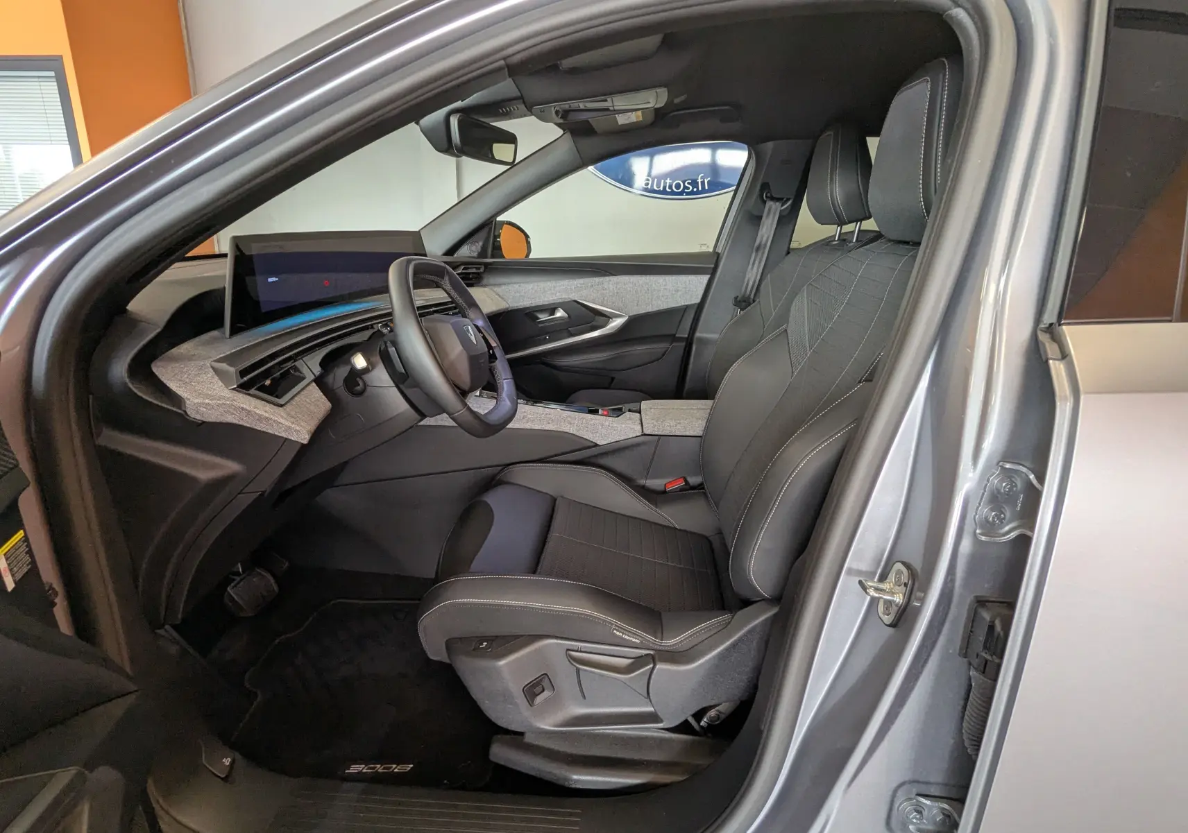 Intérieur côté conducteur du Peugeot 3008 gris 2024, avec sièges noirs, tableau de bord moderne et écran tactile.