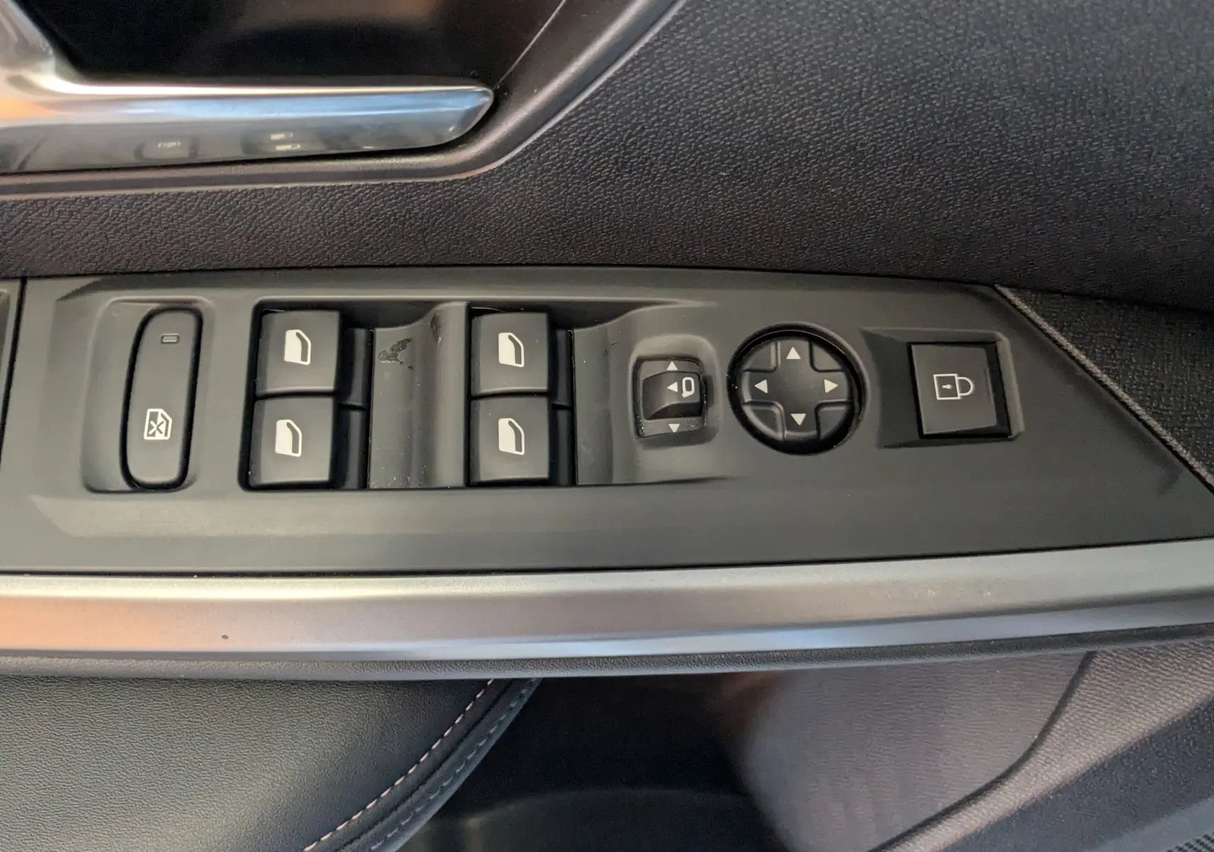 Gros plan sur les commandes des vitres et rétroviseurs côté conducteur d’un Peugeot 3008 gris, version 2024 hybride.