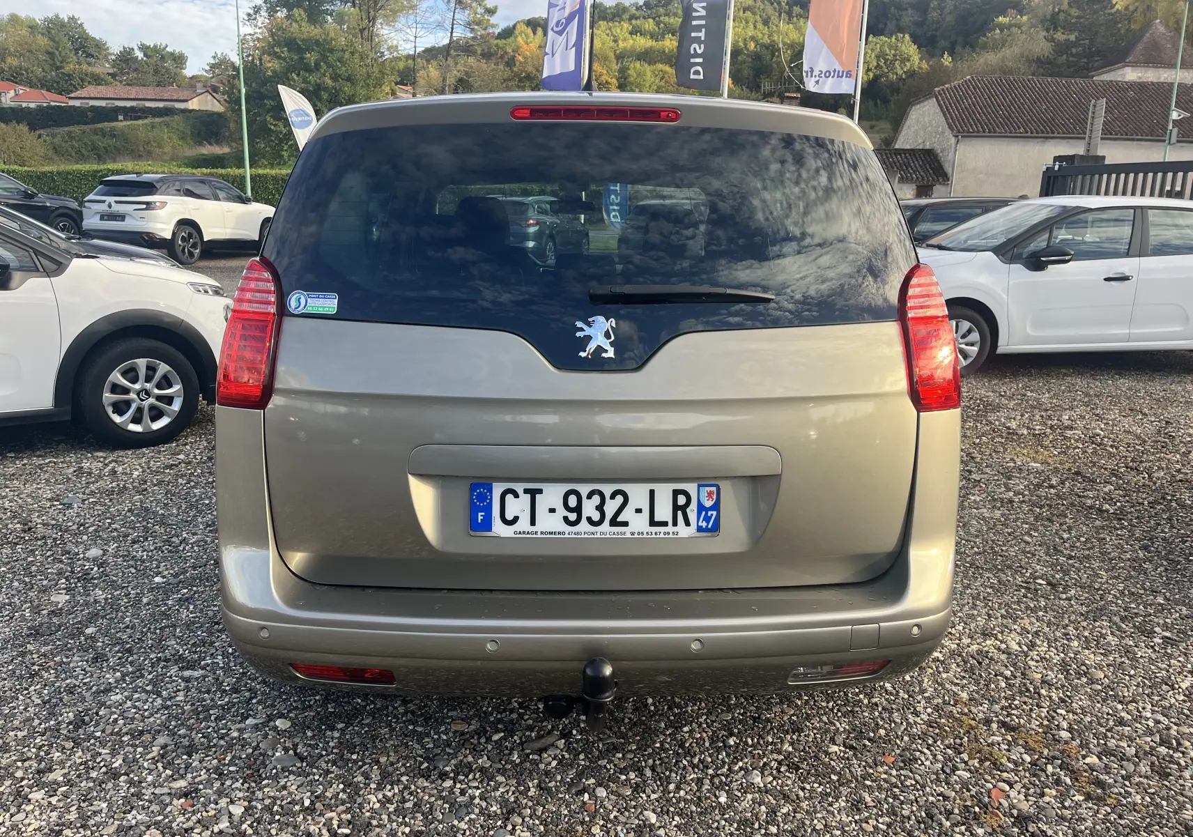 Vue arrière d'un Peugeot 5008 beige 2013 avec attelage et vitres arrière teintées sur un parking extérieur.