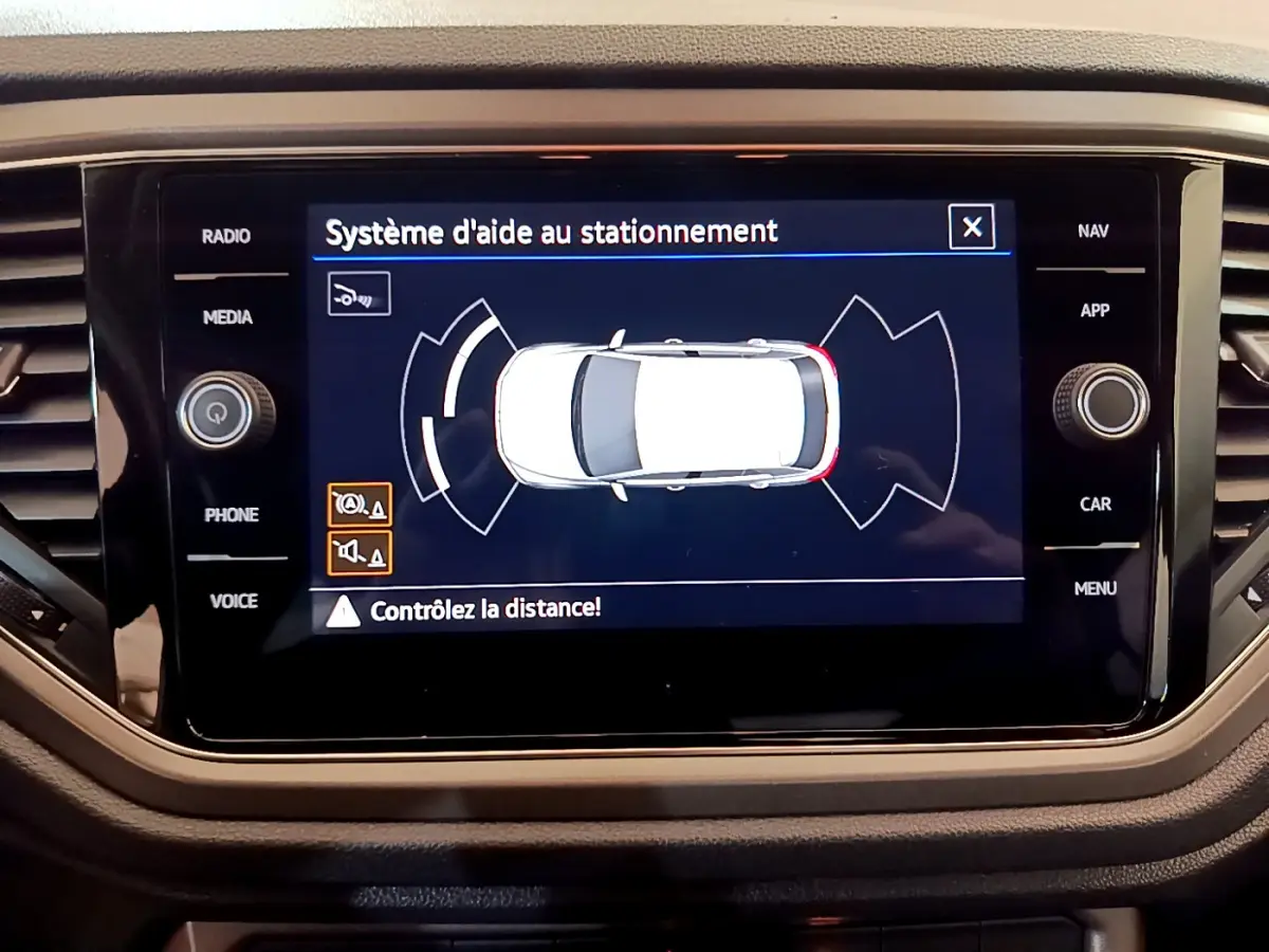 Écran tactile central du Volkswagen T-Roc gris foncé montrant le système d'aide au stationnement en vue de dessus du véhicule.