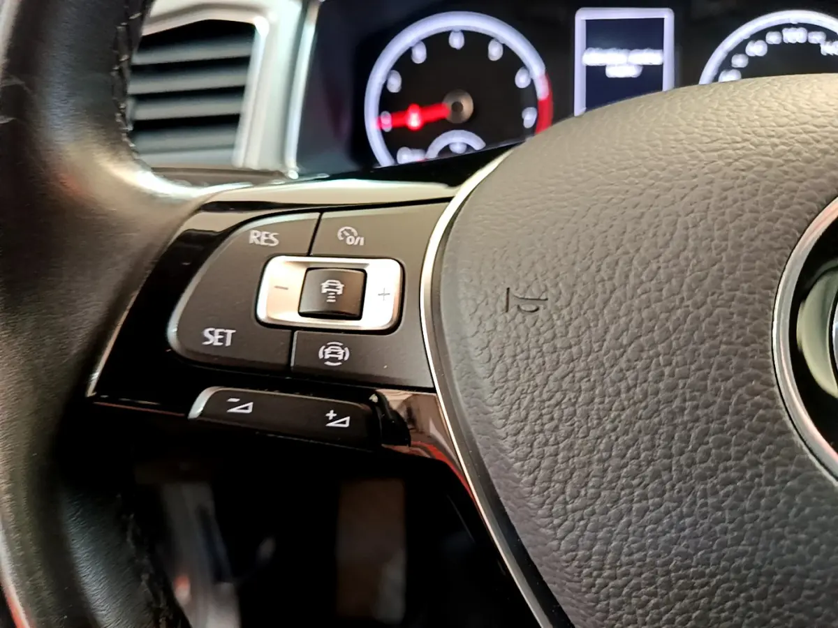 Gros plan sur le volant cuir du Volkswagen T-Roc 2021, montrant les commandes multifonctions côté gauche et le tableau de bord flou.