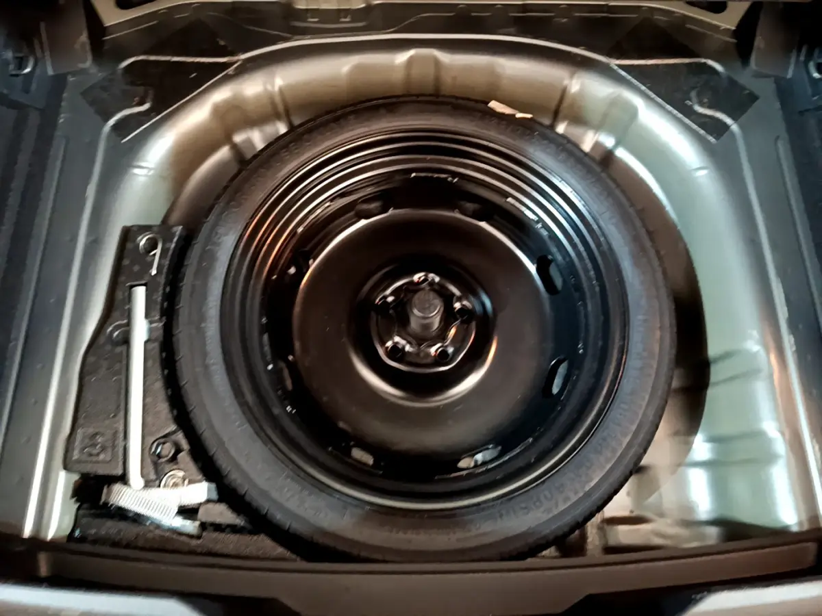 Roue de secours noire dans le coffre d'un Volkswagen T-Roc gris foncé, vue plongeante sur l'espace de rangement.