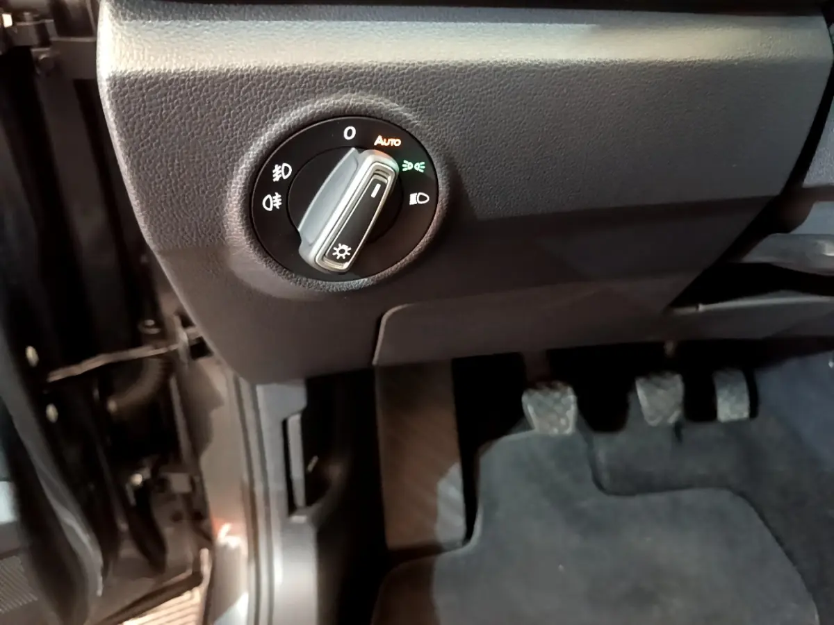 Gros plan sur le tableau de bord côté gauche du Volkswagen T-Roc gris foncé, montrant la commande des phares et les pédales.