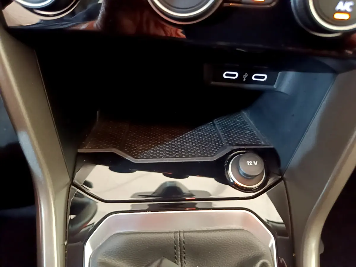 Gros plan sur la console centrale du Volkswagen T-Roc gris foncé, montrant prise 12V et ports USB éclairés.