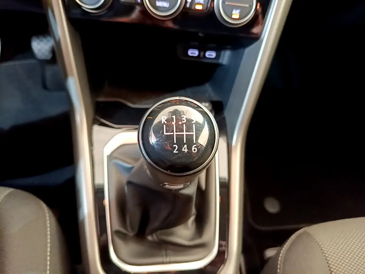 Le levier de vitesses manuel noir du Volkswagen T-Roc 1.0 TSI 110 Lounge Business vu de dessus, entouré de garnitures grises.