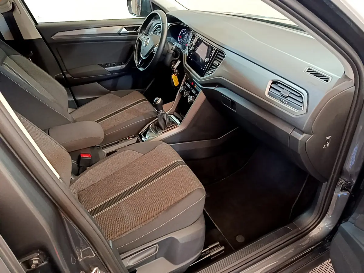 Intérieur avant droit du Volkswagen T-Roc gris foncé 2021, avec tableau de bord moderne et sièges tissu gris.