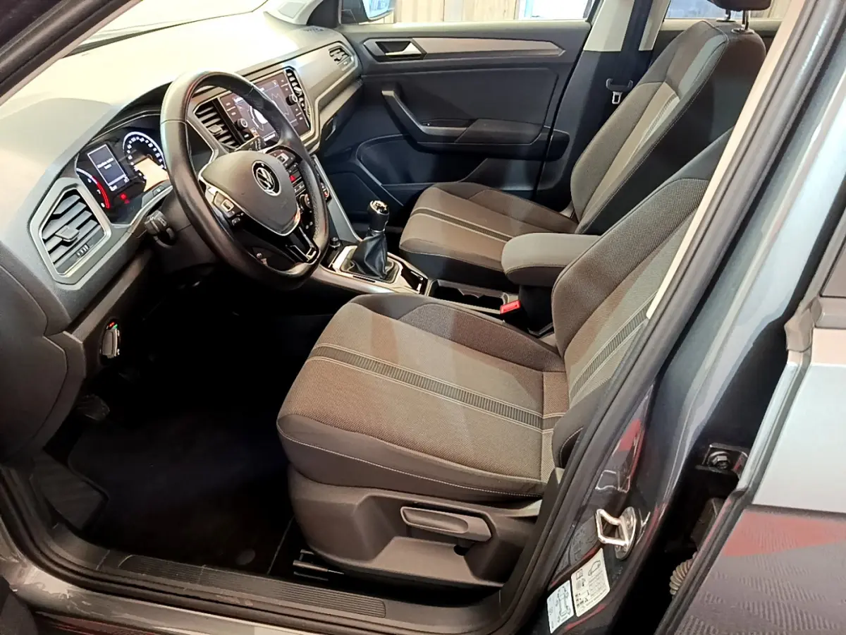 Intérieur du Volkswagen T-Roc gris foncé, vue côté conducteur, sièges tissu et tableau de bord avec écran tactile.