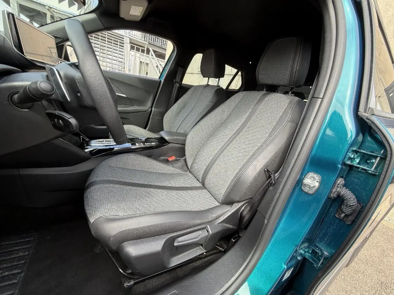 Vue intérieure côté conducteur du Peugeot 2008 2025 bleu obsession, mettant en valeur les sièges tissu et cuir gris et la console centrale.