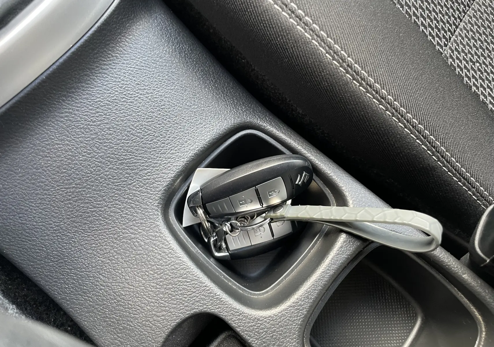 Gros plan sur la clé de contact Suzuki posée dans le rangement central noir à côté du siège tissu gris.