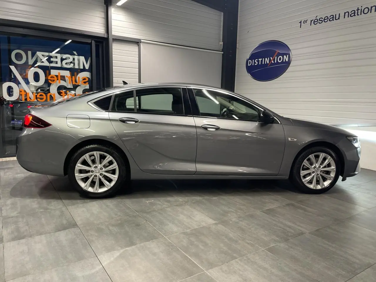 Vue latérale droite d'une Opel Insignia Grand Sport gris clair en showroom avec jantes alliage 17 pouces.