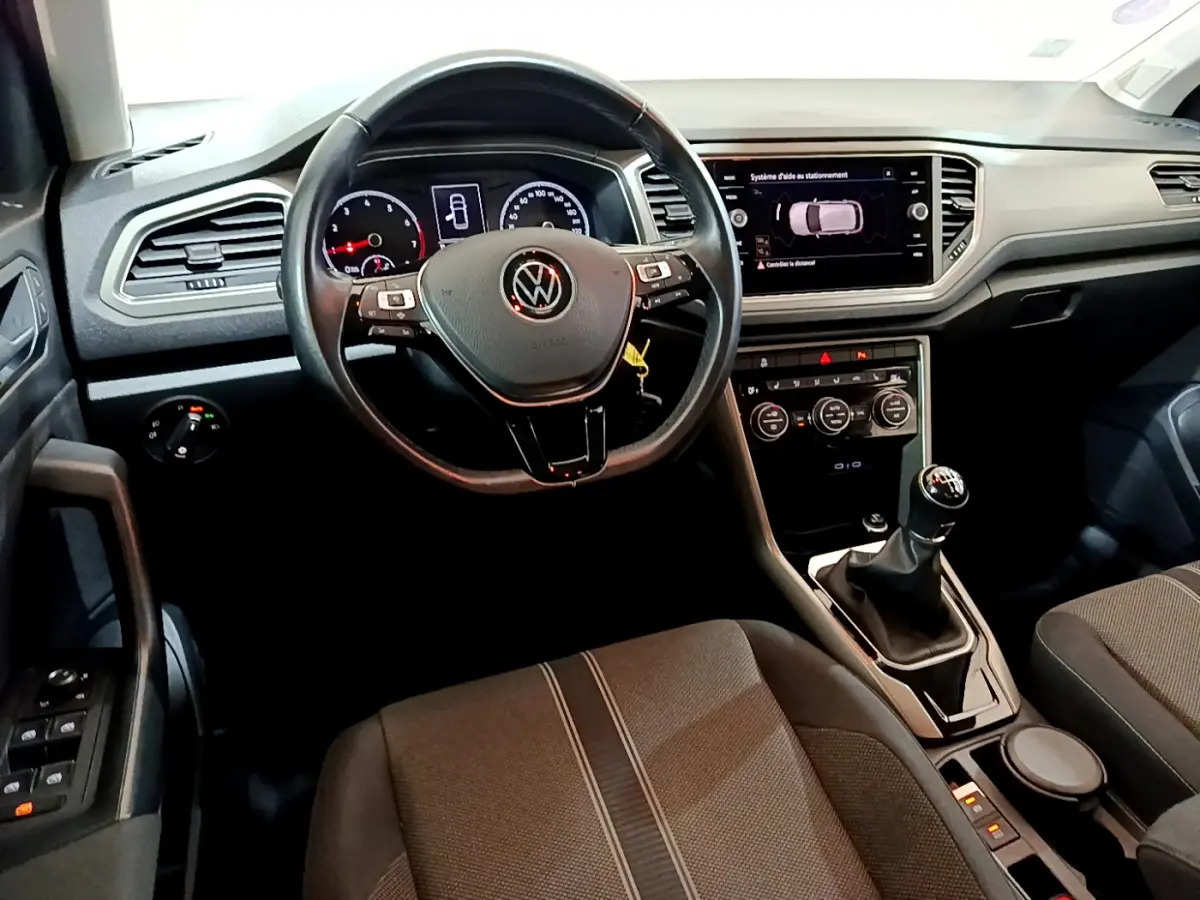 Vue intérieure du poste de conduite du Volkswagen T-Roc 1.0 TSI 110 Lounge avec volant cuir et boîte manuelle.