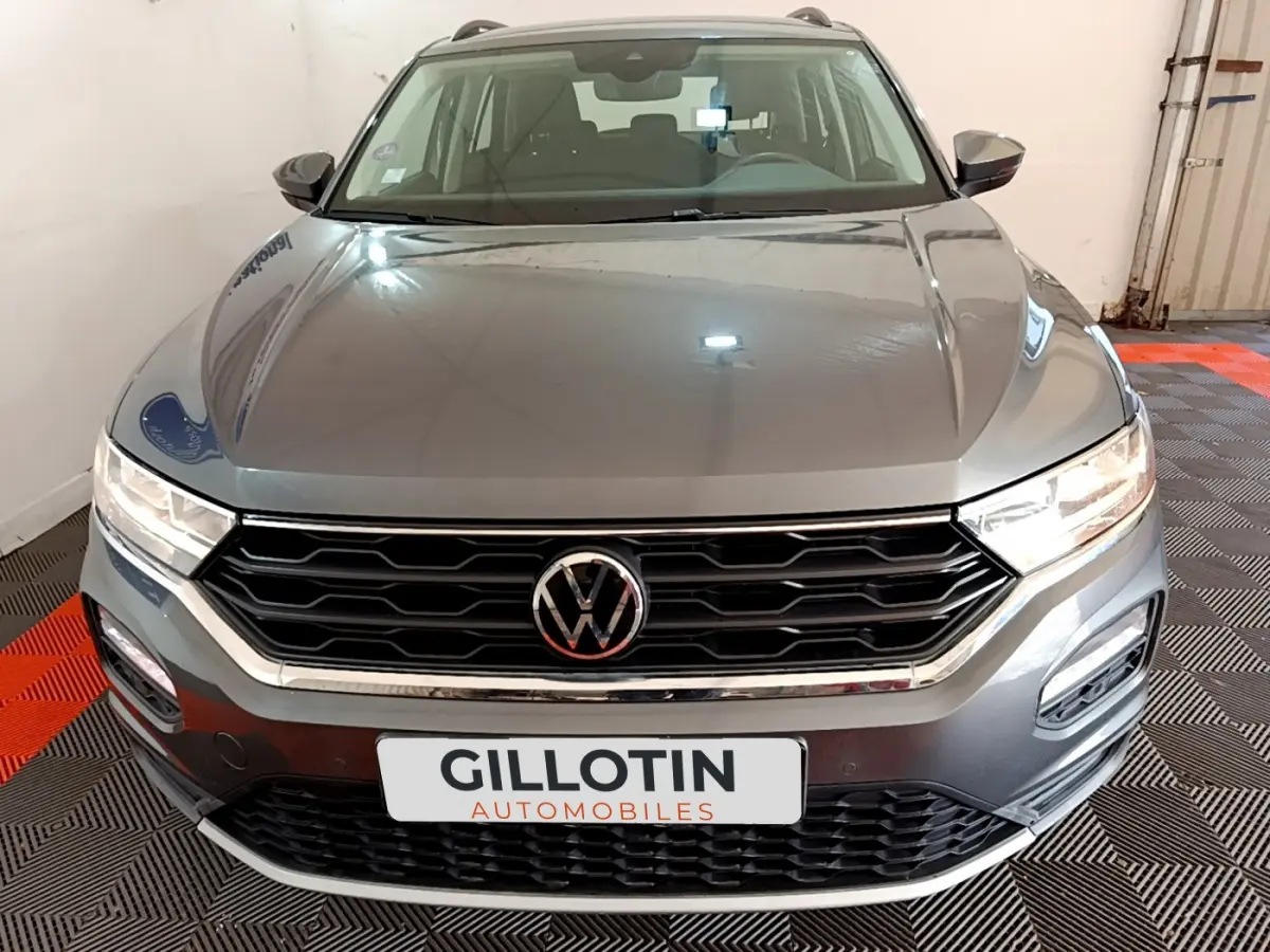 Vue frontale d'un Volkswagen T-Roc gris foncé avec calandre noire et logo VW bien visible sur fond intérieur showroom.