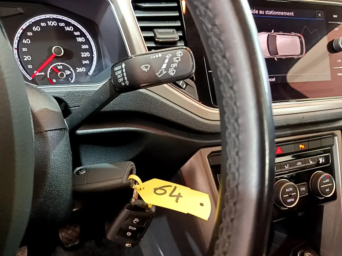 Vue intérieure rapprochée du tableau de bord et volant cuir d’un Volkswagen T-Roc 1.0 TSI 110 Lounge, avec écran tactile et clé insérée.