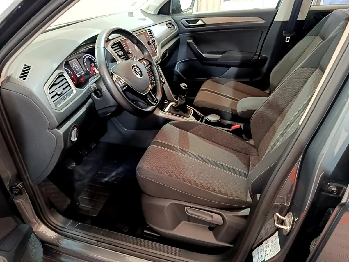 Intérieur avant droit du Volkswagen T-Roc gris foncé 2021, volant cuir, tableau de bord numérique et sièges tissu gris.