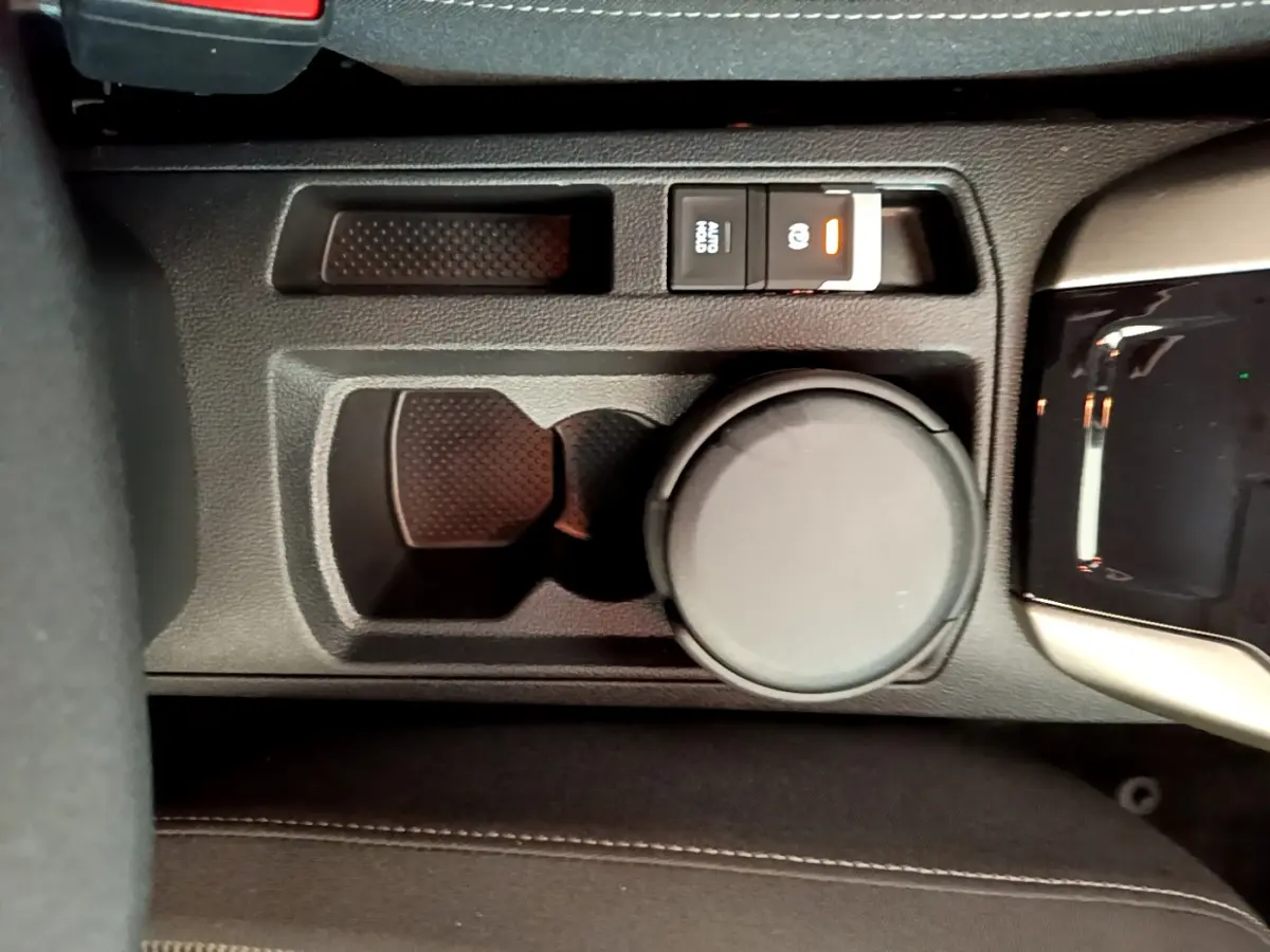 Gros plan sur la console centrale noire du Volkswagen T-Roc 1.0 TSI 110 Lounge avec frein à main électrique et porte-gobelet.