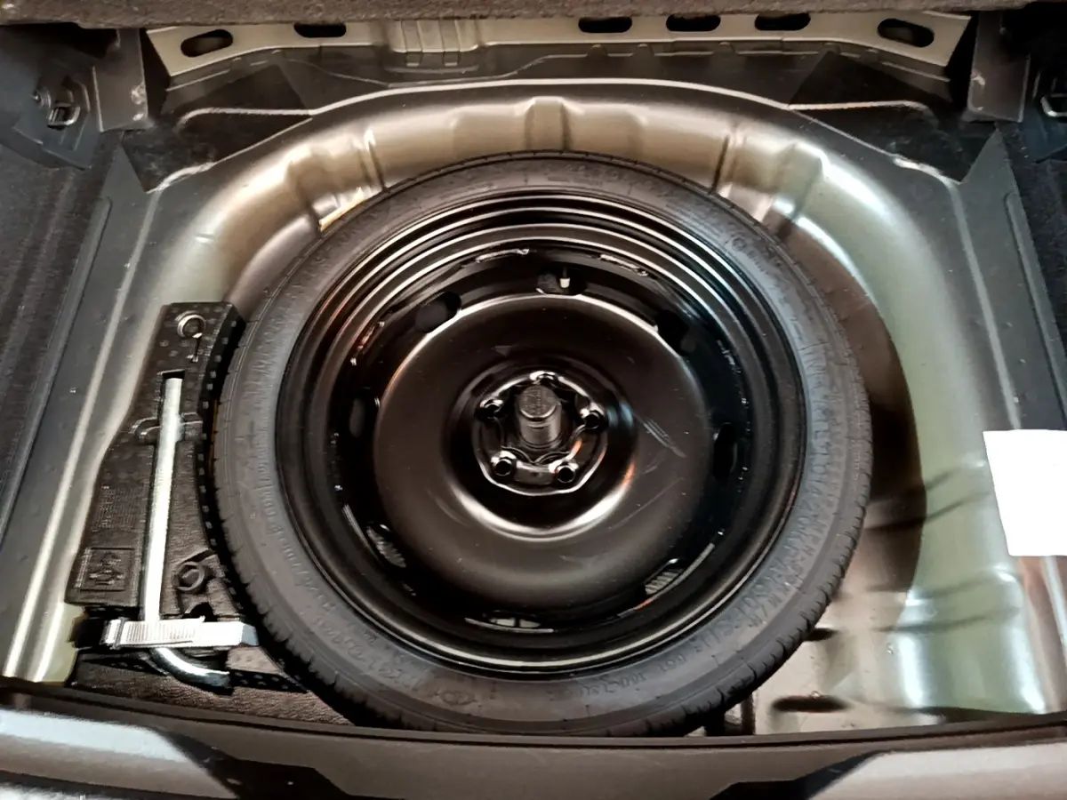 Roue de secours noire dans le coffre du Volkswagen T-Roc gris foncé, vue plongeante sur l'espace de rangement.