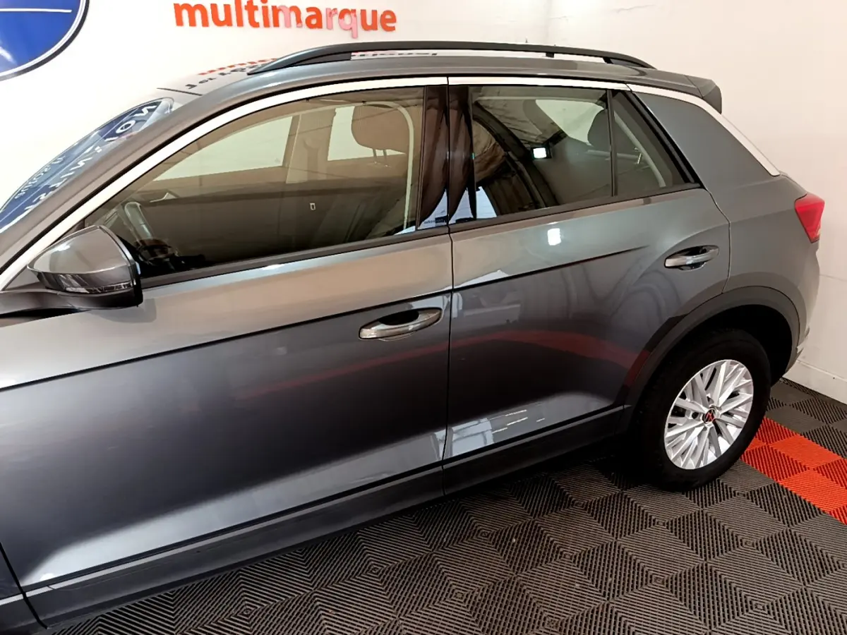 Profil côté gauche d'un Volkswagen T-Roc gris foncé, mettant en valeur les jantes et les rétroviseurs noirs avec clignotants intégrés.