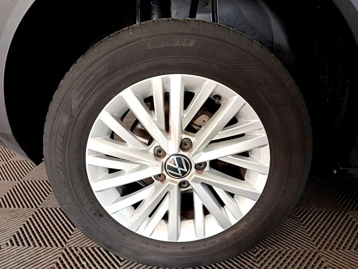 Gros plan sur la roue avant droite avec jante argentée et logo Volkswagen sur un Volkswagen T-Roc gris foncé.