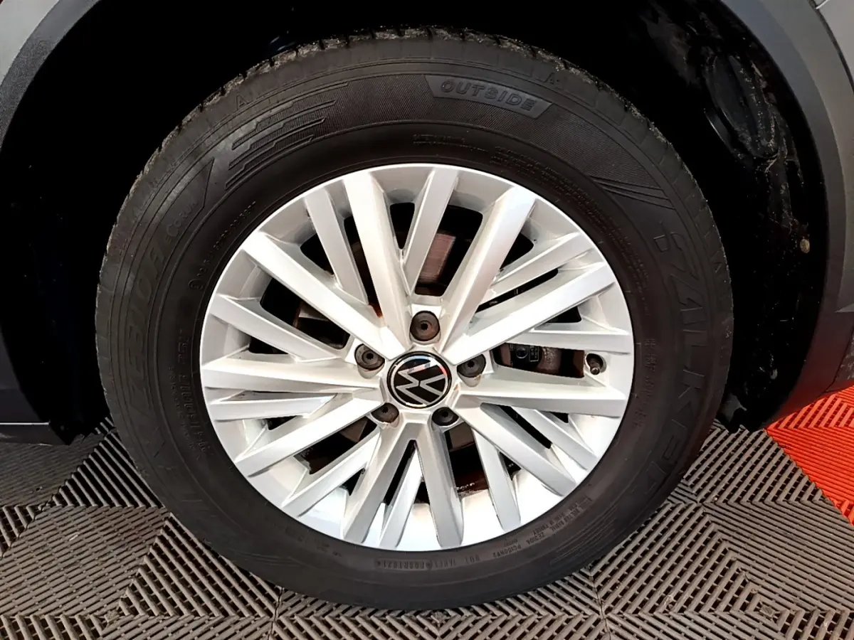 Gros plan sur la jante alliage argentée avec logo Volkswagen du côté avant droit d’un Volkswagen T-Roc gris foncé.