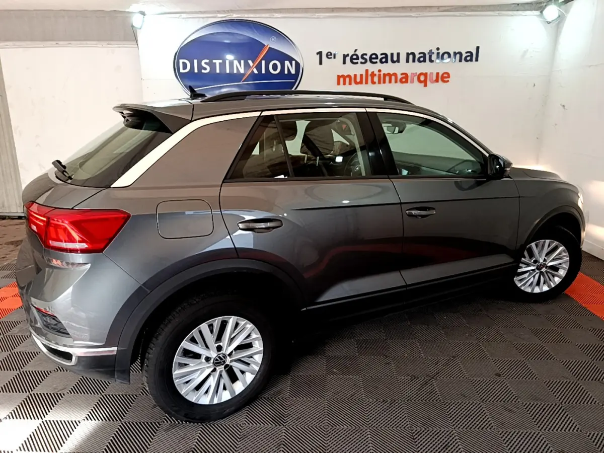 Volkswagen T-Roc gris foncé en vue profil côté gauche, avec jantes alliage et barres de toit noires visibles.