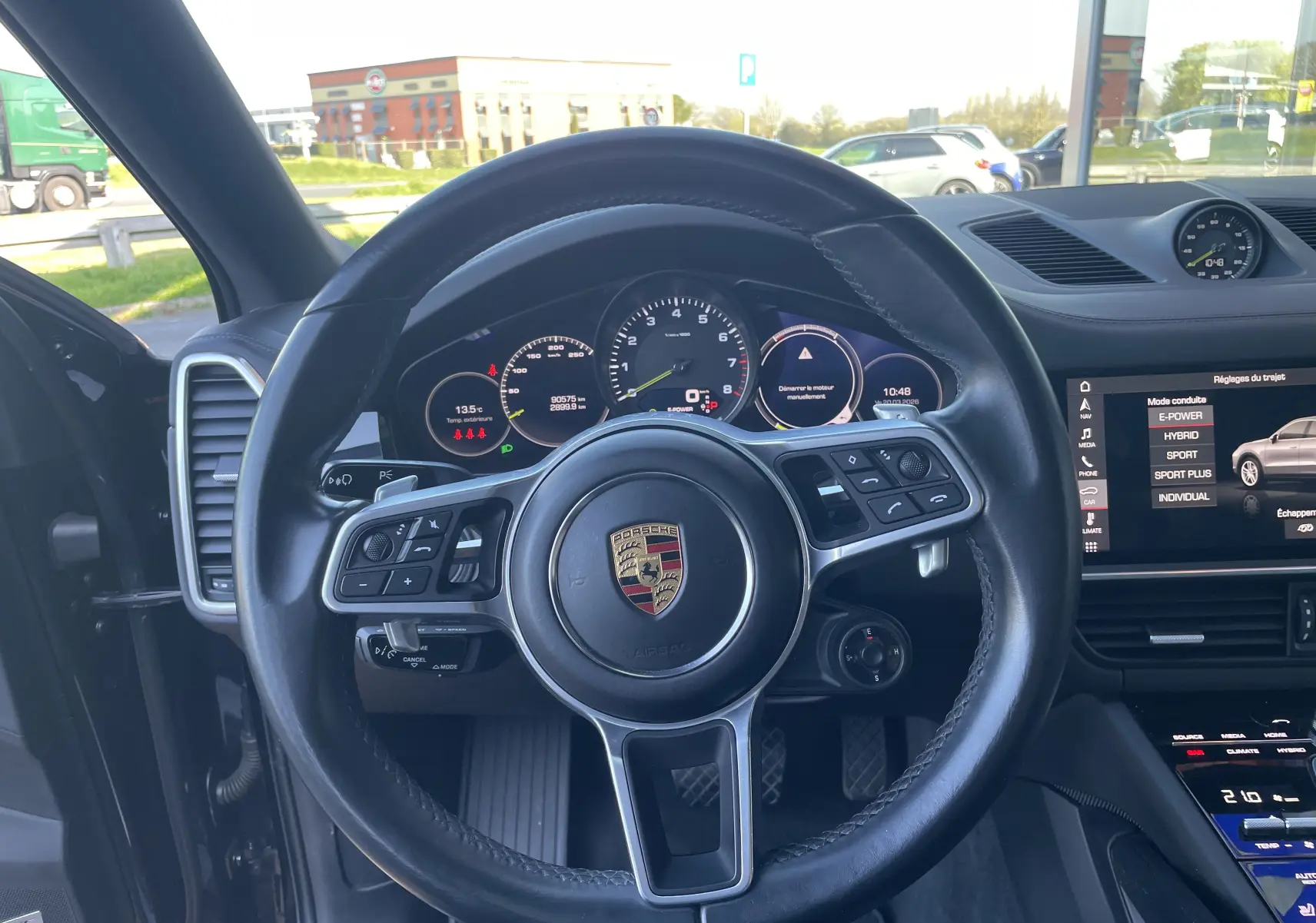 Vue intérieure centrée sur le volant cuir multifonction noir du Porsche Cayenne Coupé e-Hybrid avec tableau de bord et écran tactile.