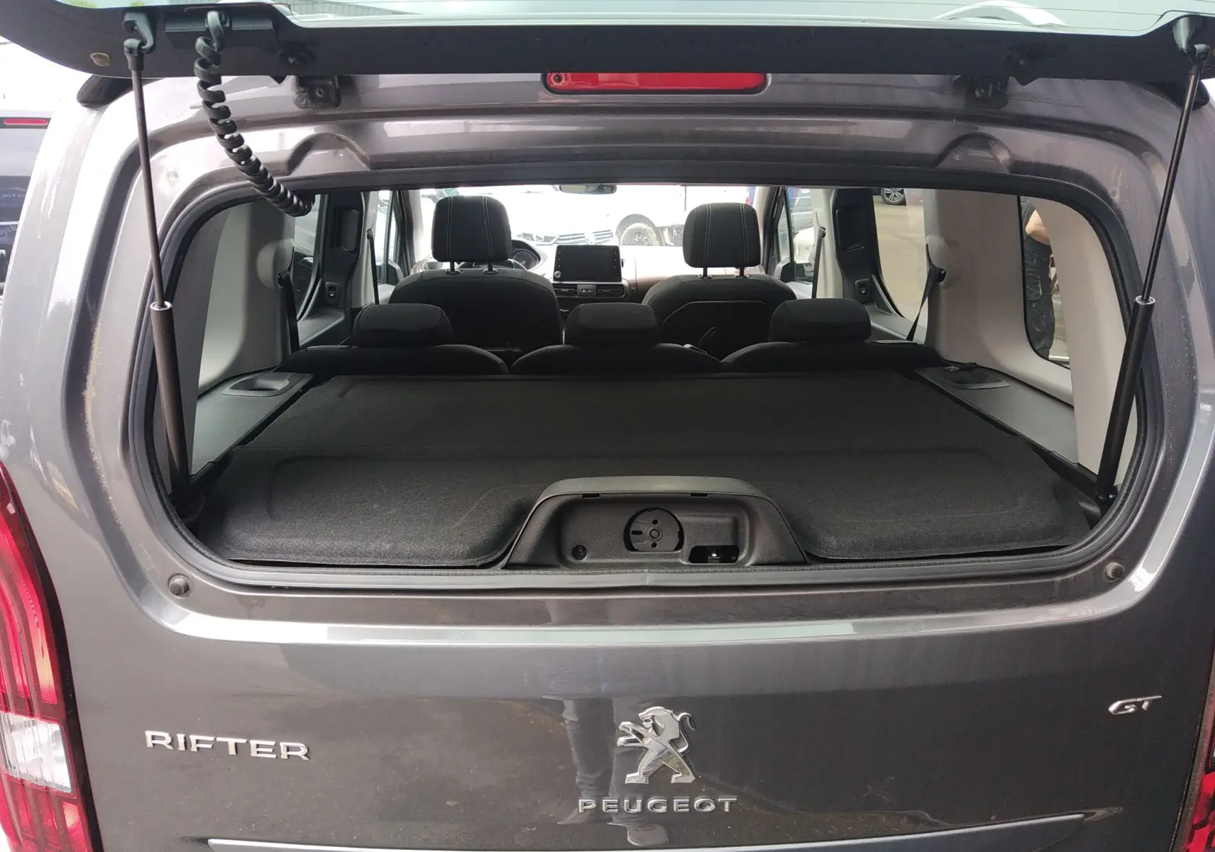 Vue arrière du Peugeot Rifter gris platinium 2022 avec hayon ouvert, montrant l'intérieur et la tablette de coffre.