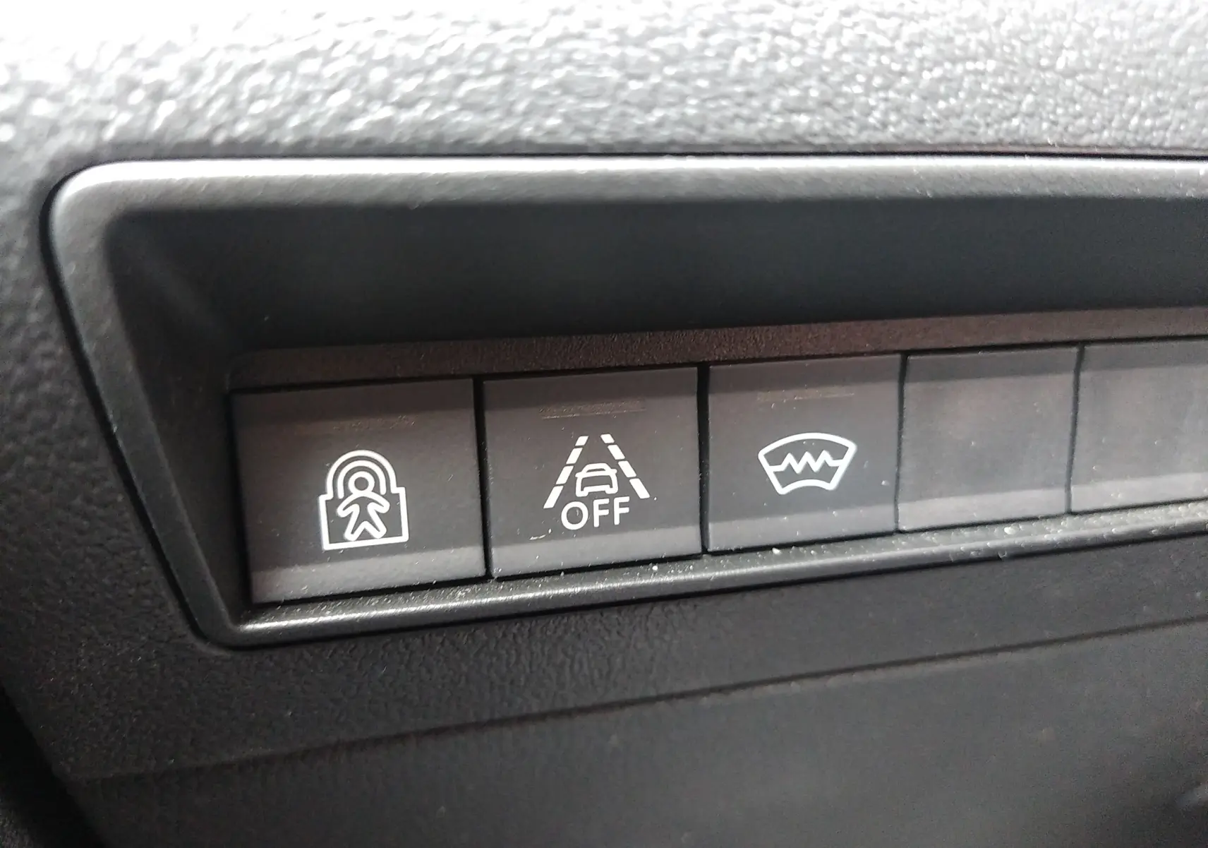 Gros plan sur les boutons de commande du tableau de bord du Peugeot Rifter gris platinium, avec symboles d’alerte et assistance.