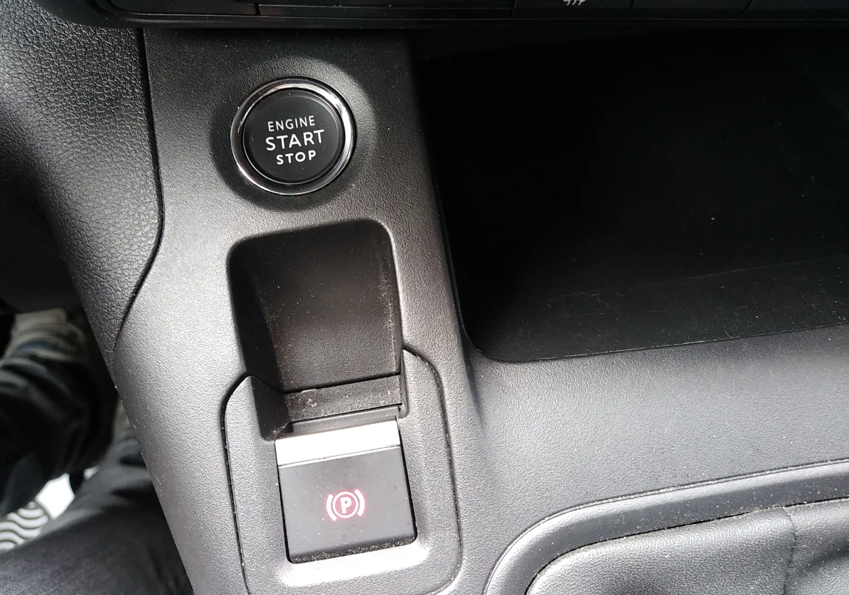 Gros plan sur la console centrale du Peugeot Rifter gris platinium 2022, montrant le bouton start/stop et le frein à main électrique.