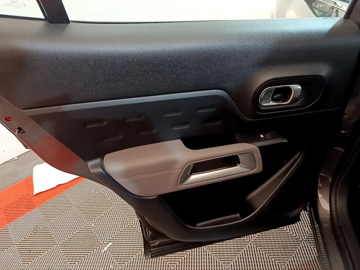 Vue rapprochée de la porte arrière gauche du Citroën C5 Aircross gris foncé, avec accoudoir clair et poignée intégrée.