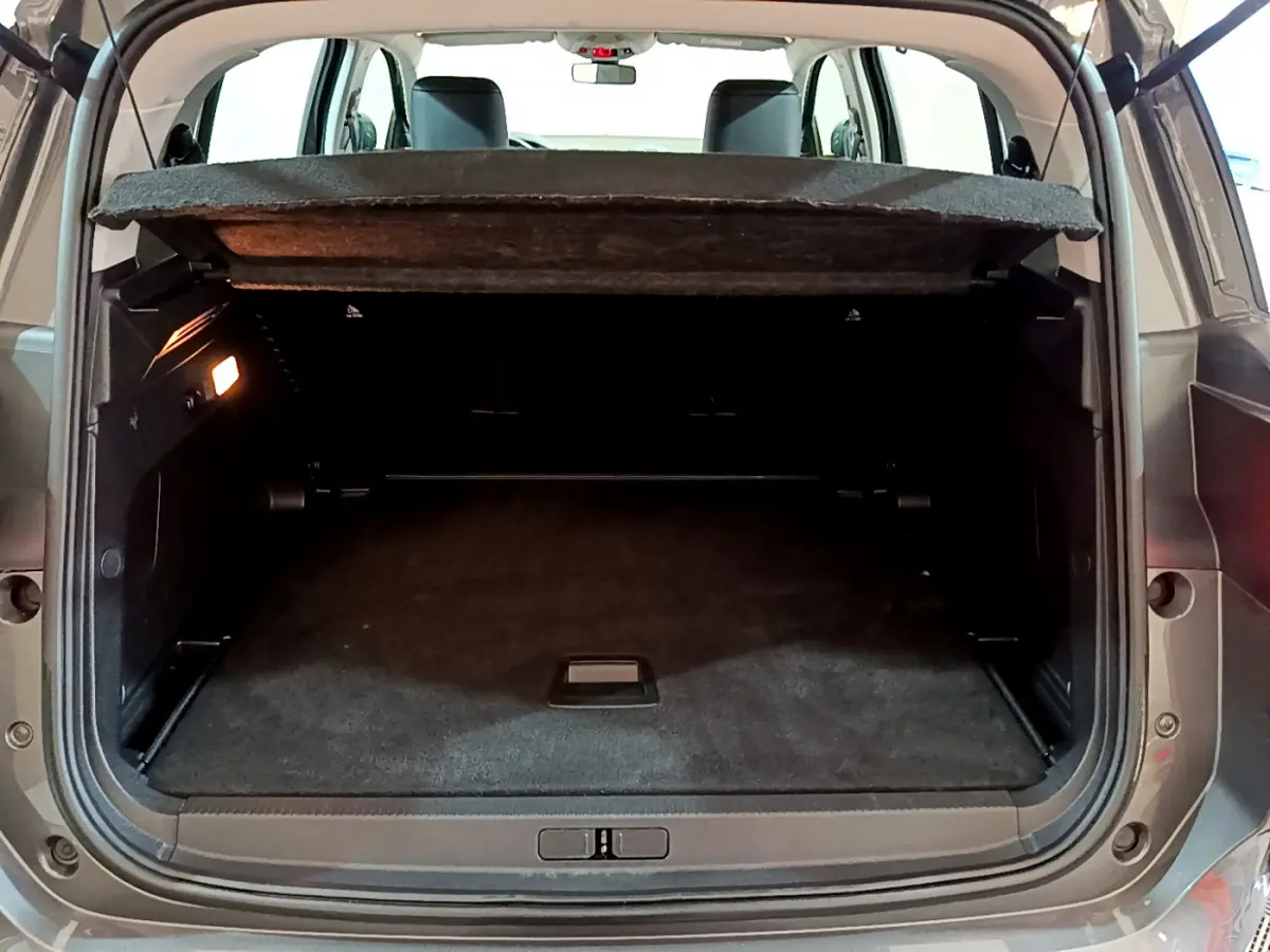 Coffre ouvert vu de l'arrière d'un Citroën C5 Aircross gris foncé avec cache-bagages relevé et éclairage intérieur allumé.