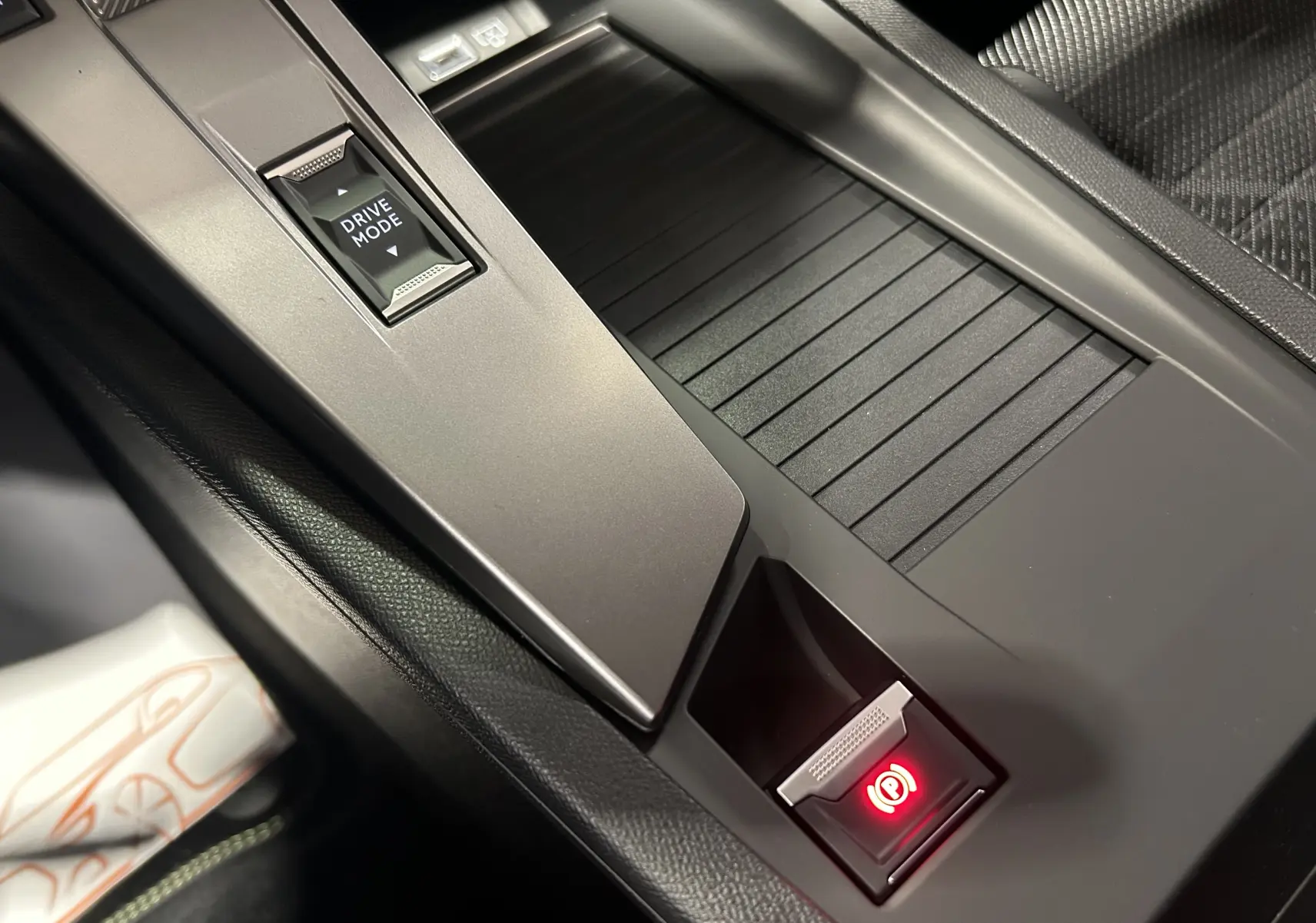 Gros plan sur la console centrale grise de la Peugeot 308 Hybrid 2026, avec bouton frein à main électronique allumé.