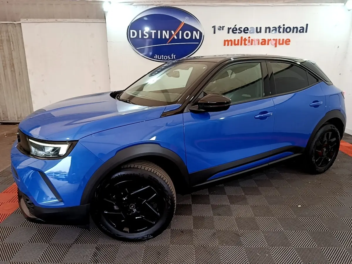 Vue 3/4 avant droite d’un Opel Mokka 2024 bleu avec toit noir et jantes noires dans un showroom.