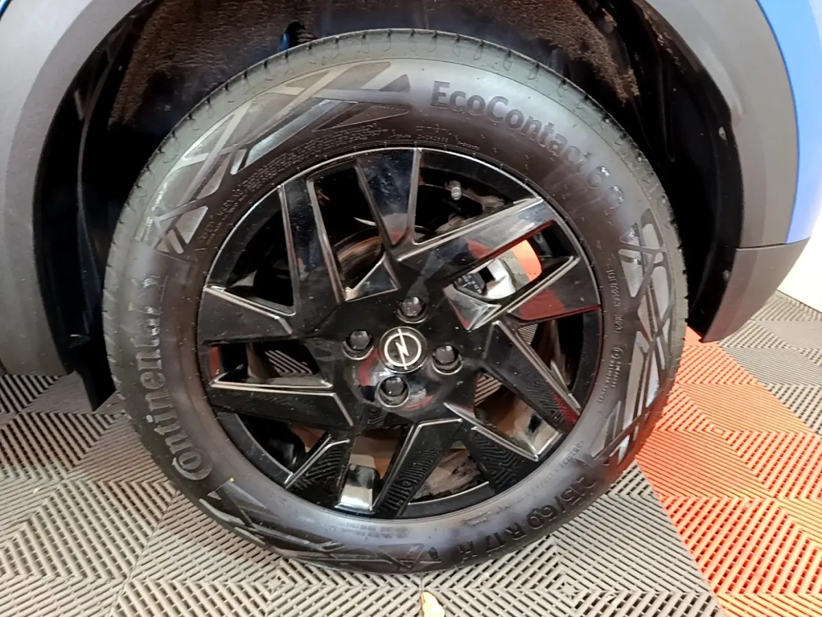 Gros plan sur la roue avant droite noire brillante de l’Opel Mokka bleu, avec logo Opel au centre.