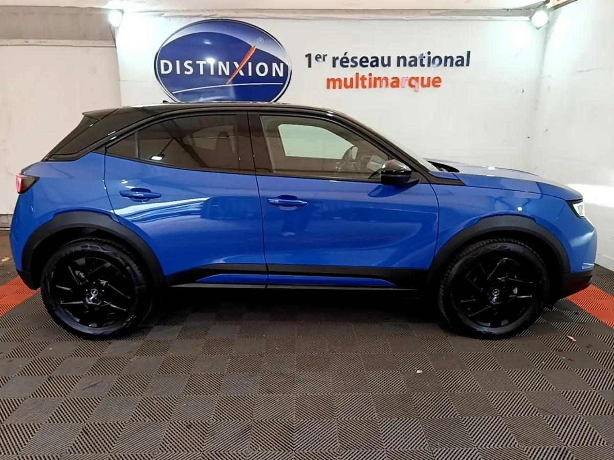 Profil latéral droit d'un Opel Mokka 1.2 Turbo 136ch GS bleu avec toit noir et jantes noires dans un showroom.