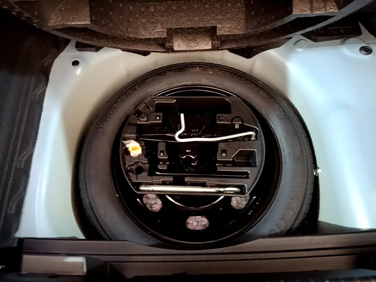 Vue plongeante sur la roue de secours noire et ses outils dans le coffre clair d’un Opel Mokka 2024.