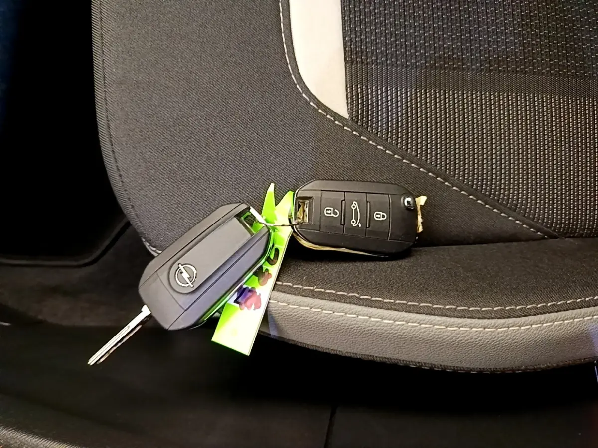 Gros plan sur deux clés Opel posées sur un siège tissu noir avec surpiqûres blanches, intérieur du véhicule visible.