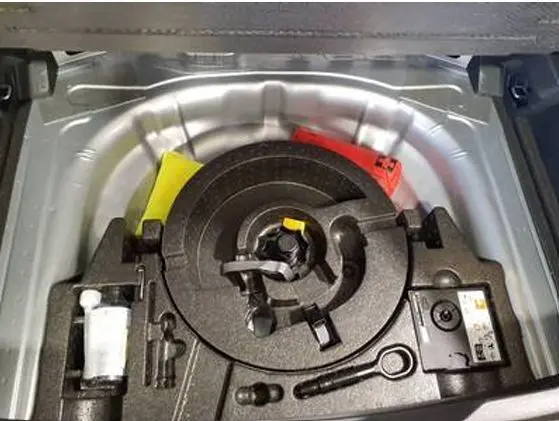 Vue rapprochée du coffre d’un Volkswagen T-Roc gris clair 2025, montrant la roue de secours et les outils de bord.