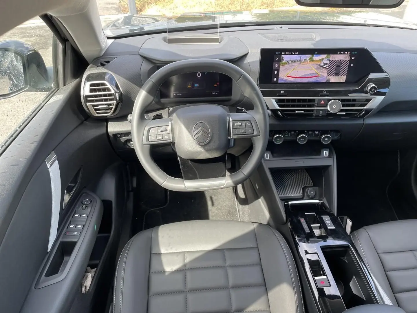 Vue intérieure avant centrée sur le volant cuir et l'écran tactile affichant la caméra de recul du Citroën C4 X noir.