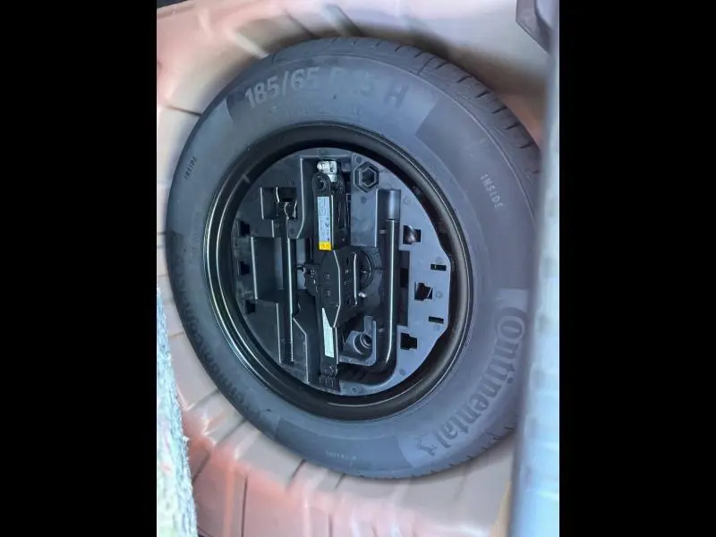 Gros plan sur la roue de secours noire et ses outils, logée dans le coffre de la Renault Clio orange 2025.