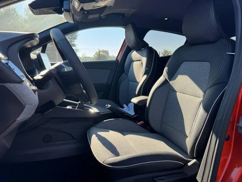 Vue intérieure côté conducteur de la Renault Clio orange 2025, sièges tissu gris avec surpiqûres blanches.
