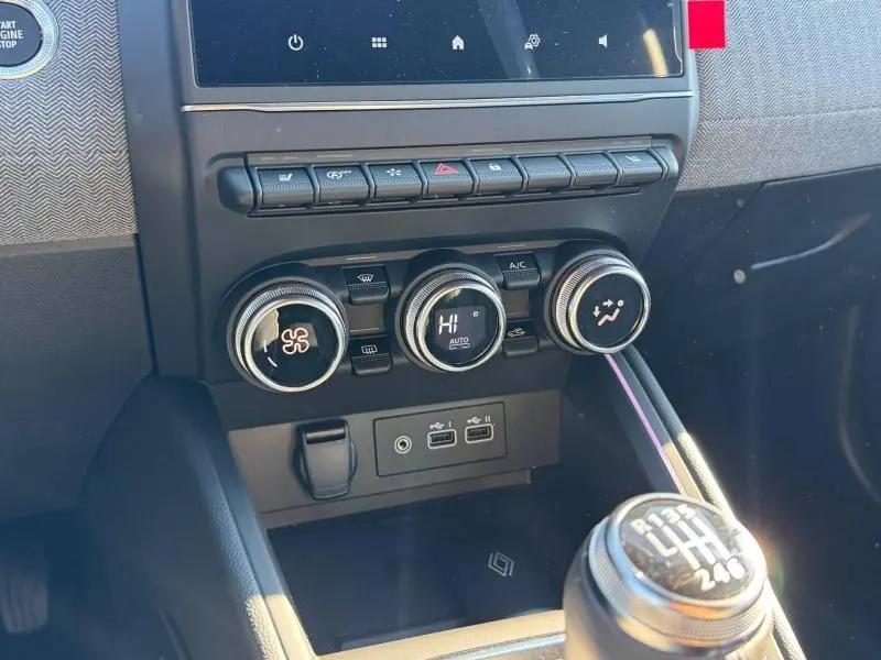 Vue rapprochée du tableau de bord et commande de climatisation de la Renault Clio orange 2025 avec levier de vitesse manuel.