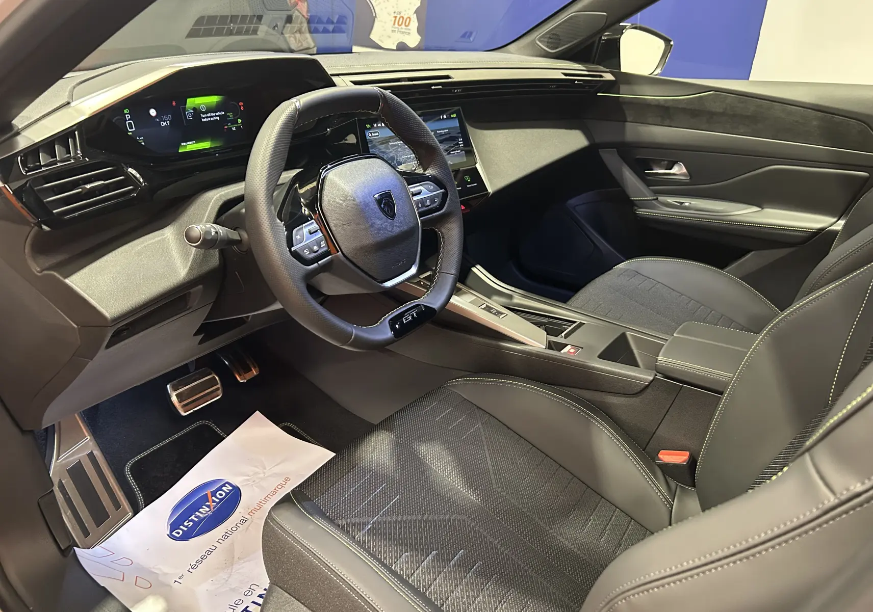 Vue intérieure côté conducteur de la Peugeot 308 HYBRID 145 GT avec tableau de bord numérique et volant compact cuir noir.