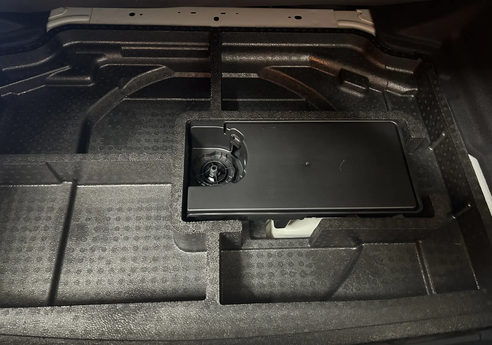 Gros plan sur le rangement en mousse noire sous le coffre de la Peugeot 308 III Ph.2 Hybrid 145 GT blanc Okenite.